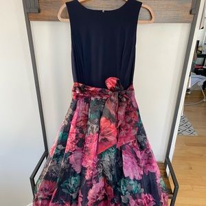 Floor length, floral, sleeveless gown with sash and navy blue top.